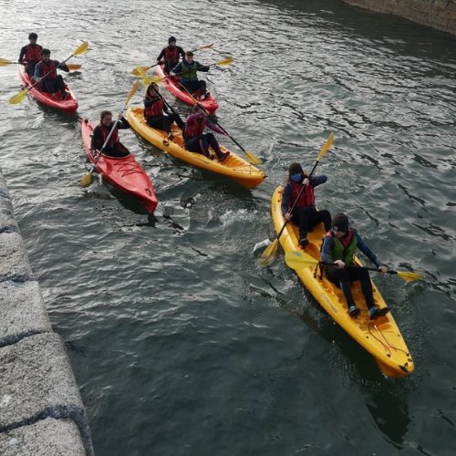 Kayakers in yellow and red kayaks traverse a narrow canal.
